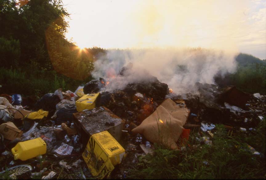 large pile burning farm trash with many plastics and herbicide jugs visible